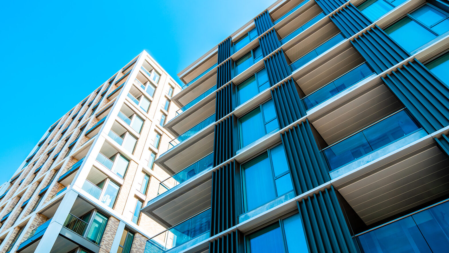 Modern apartment buildings with large windows and balconies rise against a bright blue sky, part of a sought-after landed estate.